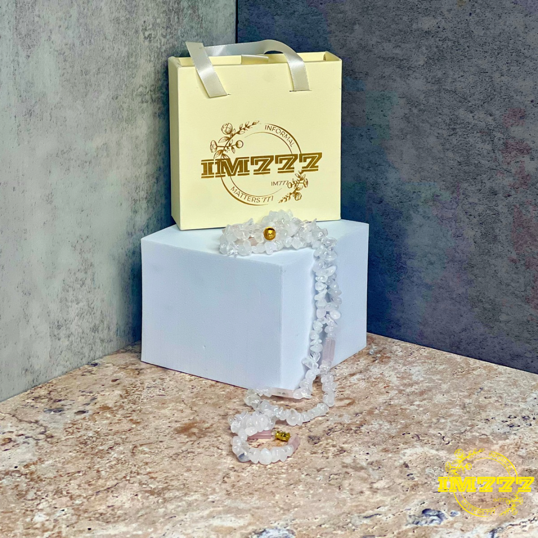 A waist bead made of clear and rose quartz stones, displayed in front of a branded packaging with the text 'IM777'.